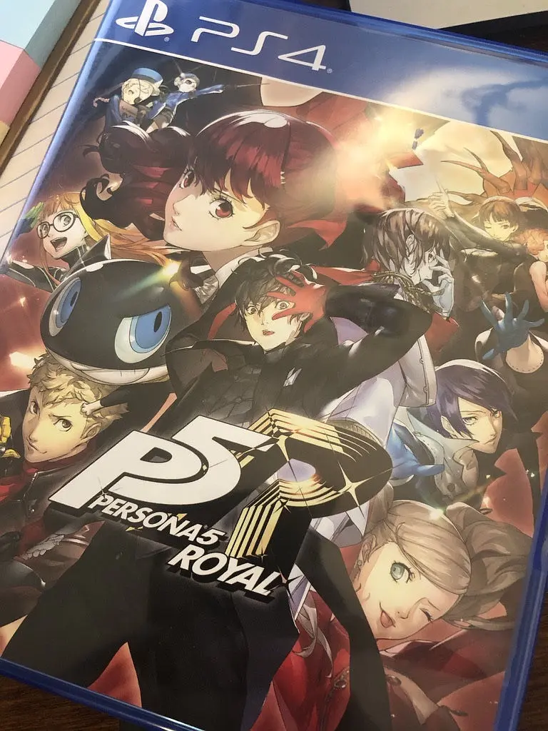 PS4 版《Persona 5 Royal》的实体盘,放在书桌的本子上